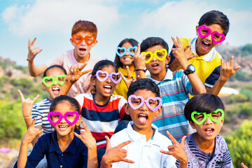 Group of kids cheering with wearing colourful glasses by looking at camera during summer camp of...