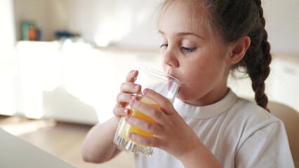girl child drinking juice. happy family a healthy eating kid dream concept. daughter girl drinking yellow juice from a glass cup in indoor the kitchen. child drinking fruit juice