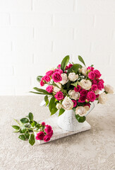 Fototapeta na wymiar a beautiful bouquet of fresh garden roses in a decarative vase in the form of a watering can. concrete table against a white brick wall.