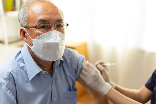Medical worker perform a vaccine injection to senior Asian man in clinic or medical facility.