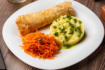 Crispy pork chop served with warm potato puree sprinkled with green onion and carrot salad, on a white plate on a wooden table.