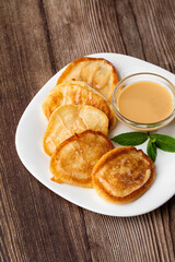 Pile of freshly fried thick pancakes, in Eastern European cuisines called oladky or oladyi with condensed milk on wooden background
