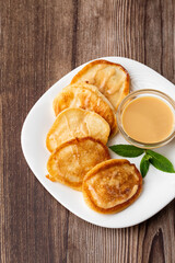 Pile of freshly fried thick pancakes, in Eastern European cuisines called oladky or oladyi with condensed milk on wooden background