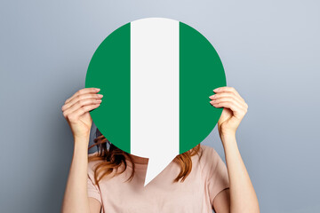 student girl holds blank white speech bubble with Nigeria flag isolated over grey studio...