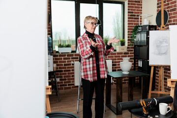 Elder teacher explaining sketching technique to multiethnic art students during creative workshop. Diverse team learning how to sketch model on canvas using graphic pencil. New years resolutions