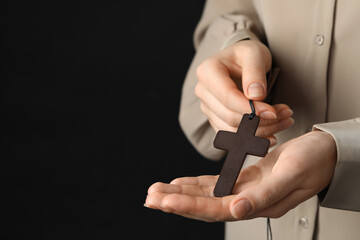 Fototapeta premium Woman holding wooden Christian cross on black background, closeup. Space for text