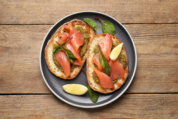 Delicious bruschettas with salmon and pesto sauce on wooden table, top view