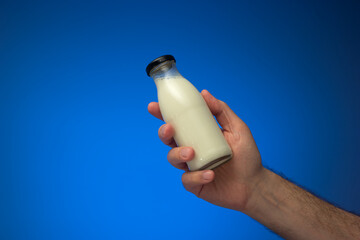 Small glass milk bottle with cap held in hand by Caucasian male. Close up studio shot, isolated on...