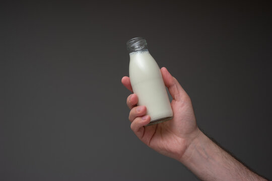 Small glass milk bottle with cap held in hand by Caucasian male. Close up studio shot, isolated on gray background