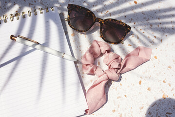 Top view of sunglasses and a scrunchie on a notebook in sunlight