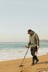 A man with a metal detector and a shovel on the seashore. A treasure hunter with a metal detector. A man is looking for a treasure.