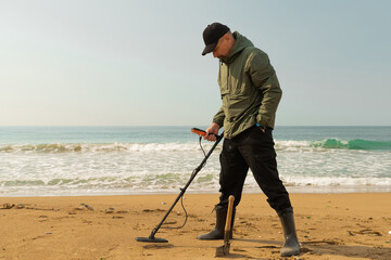 A man with a metal detector and a shovel on the seashore. A treasure hunter with a metal detector. A man is looking for a treasure.