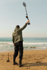 A man with a metal detector and a shovel on the seashore. A treasure hunter with a metal detector....