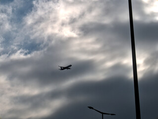 Silhouette of an airplane above the city preparing to land. Dramatic cloudy sky in the background