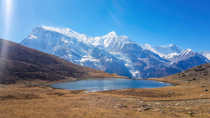 Fototapeta na wymiar Ice lake, as part of the Annapurna Circuit Trek detour, Himalayas, Nepal. Annapurna chain in the back, covered with snow. Clear weather, dry grass, snowy peaks. Freedom, solitude, chill and relaxation