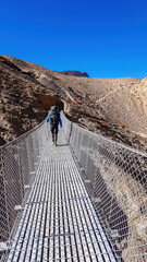 A man crossing through a suspension bridge in Himalayas. The valley is located in Mustang region,...
