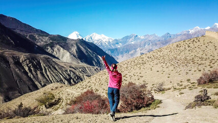 Eine Frau genießt den Blick auf das trockene Himalaya-Tal in der Mustang-Region, Annapurna Circuit Trek in Nepal. Im Hintergrund befindet sich der schneebedeckte Dhaulagiri I. Karge und steile Hänge. Harter Zustand.