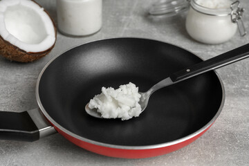 Frying pan with coconut oil and spoon on light grey table