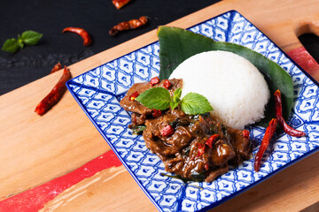 Asian Food concept Thai holy Basil Beef Stir Fry and Jasmine Rice Khao Pad Pad Kra Pow Nua in Thai tradition ceramic plate on wooden board and black slate stone background with copy space - obrazy, fototapety, plakaty