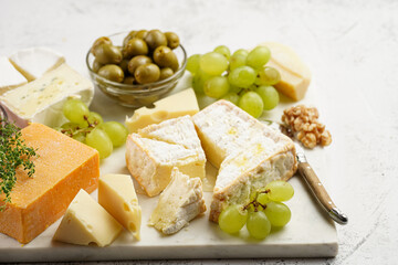 Cheese platter with organic cheeses - blue cheese cheddar, emmantaler, french soft cheese with strong smell, italian parmesan, grapes, tomatoes, olives, nuts and crackers on marble board