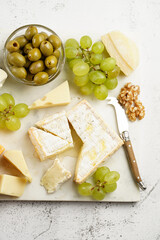 Cheese platter with organic cheeses - blue cheese cheddar, emmantaler, french soft cheese with strong smell, italian parmesan, grapes, tomatoes, olives, nuts and crackers on marble board