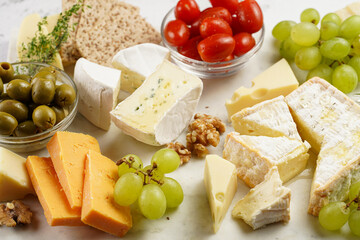 Cheese platter with organic cheeses - blue cheese cheddar, emmantaler, french soft cheese with strong smell, italian parmesan, grapes, tomatoes, olives, nuts and crackers on marble board