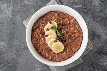 Chocolate oatmeal porridge with banana and chocolate chips on top in a white bowl. Healthy...