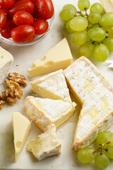 Cheese platter with organic cheeses - blue cheese cheddar, emmantaler, french soft cheese with strong smell, italian parmesan, grapes, tomatoes, olives, nuts and crackers on marble board