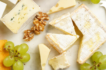 Cheese platter with organic cheeses - blue cheese cheddar, emmantaler, french soft cheese with strong smell, italian parmesan, grapes, tomatoes, olives, nuts and crackers on marble board