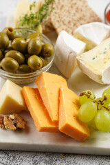 Cheese platter with organic cheeses - blue cheese cheddar, emmantaler, french soft cheese with strong smell, italian parmesan, grapes, tomatoes, olives, nuts and crackers on marble board
