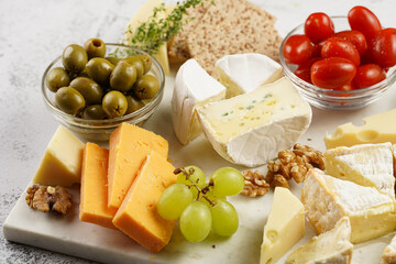 Cheese platter with organic cheeses - blue cheese cheddar, emmantaler, french soft cheese with strong smell, italian parmesan, grapes, tomatoes, olives, nuts and crackers on marble board