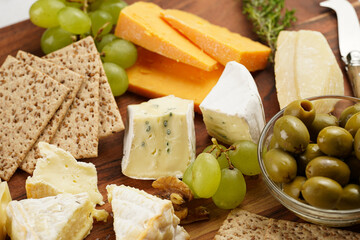 Cheese platter with organic cheeses - blue cheese cheddar, emmantaler, french soft cheese with strong smell, italian parmesan, grapes, tomatoes, olives, nuts and crackers on wooden board