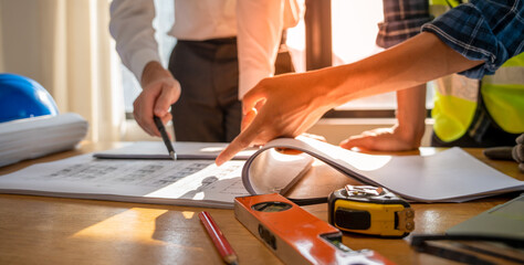 Focused at the desk. behind is engineer and construction team leaders work together. View house...
