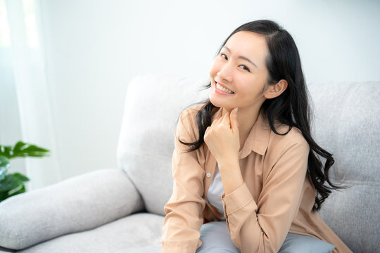 A smiling and laughing Asian teenage woman is happy inside the living room. Young students feel relaxed, at ease, think positive.