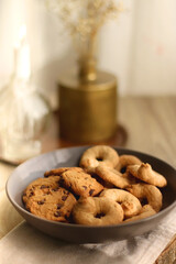 Bowl of sugar cookies and chocolate chip cookies, lit candle and vase with flowers on the table. Selective focus.