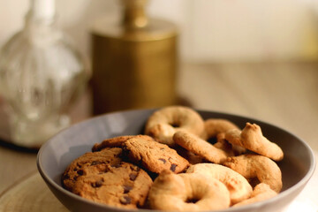 Bowl of sugar cookies and chocolate chip cookies, lit candle and vase with flowers on the table. Selective focus.