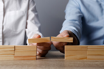 Businesspeople building bridge with wooden blocks at table, closeup. Connection, relationships and deal concept