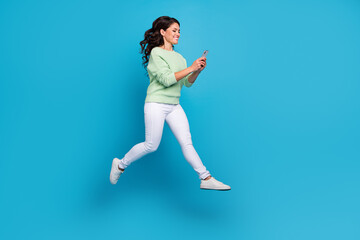 Fototapeta na wymiar Full body photo of impressed young brunette lady run with telephone wear shirt pants shoes isolated on blue background