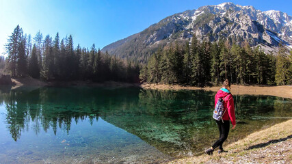Woman enjoying a peaceful Green Lake, located in an Alpine valley in Austria. The algae in the lake give it its distinctive color. Lots of pine trees on the shore. The girl is walking along the lake.
