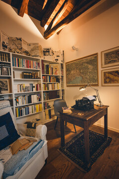 An old classic typewriter in a vintage style studio with a wooden desk lit by a lamp, wit old books all around. A moody, dark atmosphere for a writer working at night.