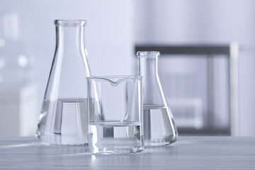 Different laboratory glassware with transparent liquid on wooden table against blurred background. Space for text