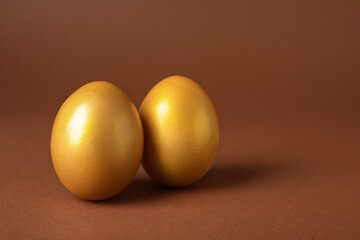 Shiny golden eggs on brown background, closeup. Space for text