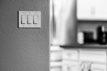 Closeup of a bank of light switches with a kitchen in the blurry background in grayscale