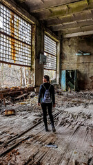 Girl in black outfit walks around the rotten floor in an abandoned sports hall in Pripyat, Ukraine,...