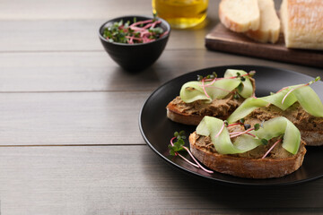 Slices of bread with delicious pate, cucumber and microgreens on wooden table, space for text
