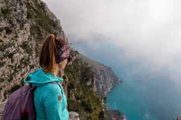Naklejka premium Woman with scenic view from a hiking trail on the coastal driving road of beautiful Amalfi Coast, Campania, Italy, Europe. Riviera coastline at Mediterranean sea. Panoramic curvy road near Positano