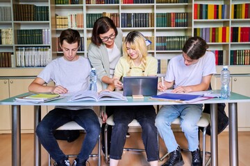 Group of teenage students studying in library class with female teacher mentor