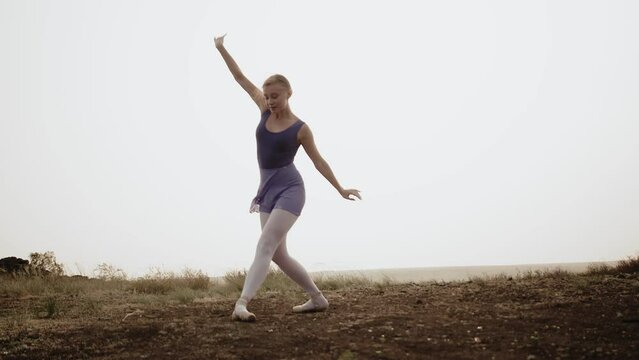 Beautiful ballerina dances on pointe shoes outdoor. Dancer slowly dances in field on pointe shoes. Concept of classical dance and art