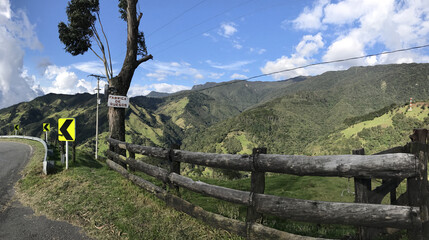 Panoramic shot of green mountains in the side of a road with a blue sky on horizon on a sunny day - Powered by Adobe