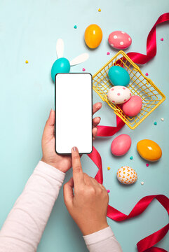 Adult hands holding smartphone with colorful Easter eggs, red ribbon and small yellow basket